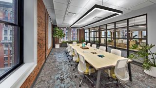 Conference table with overhead light and greenery plant decor in brick building.